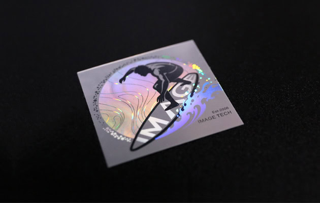 Achromatic white optical label featuring a surfer, with flowing structural colors revealed under changing light